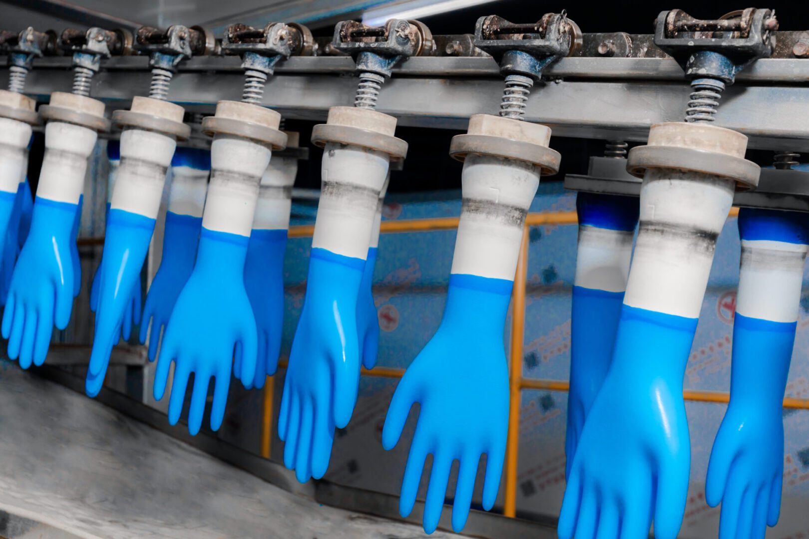 Medical rubber gloves production line, factory interior environment Blue rubber gloves on a production line, hanging upside down on metal molds in a factory setting.