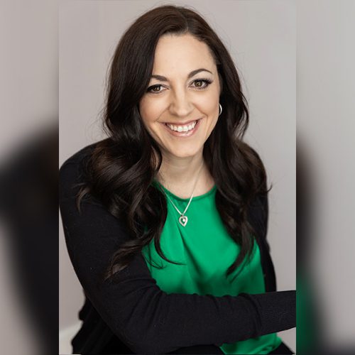 Patricia headshot Smiling woman with long dark hair wearing a green top and necklace, seated against a neutral background.